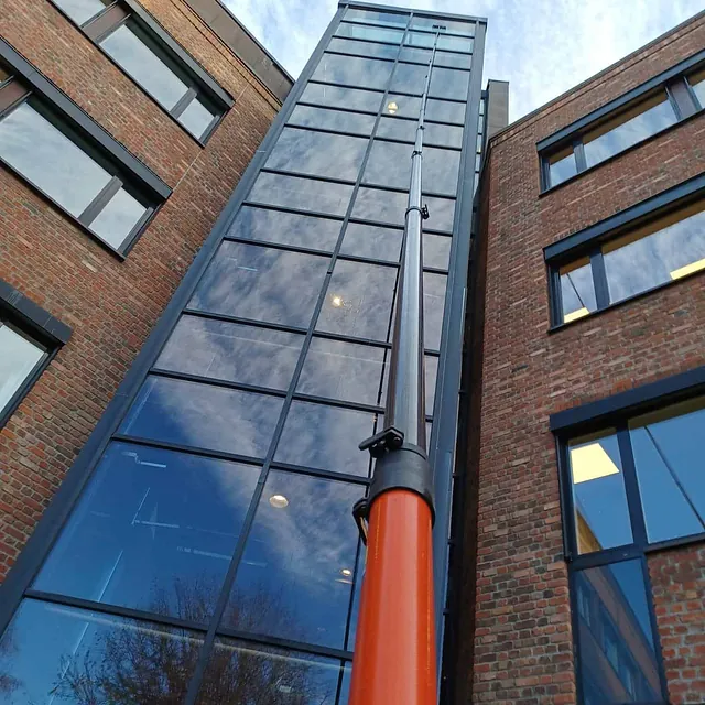Teleskopstang i bruk for å vaske høye glassfasader på murbygning.