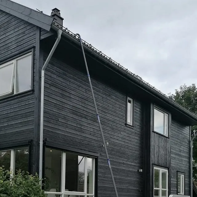 Høyt sort hus med teleskopstang brukt til vask av takrenne eller vegg.
