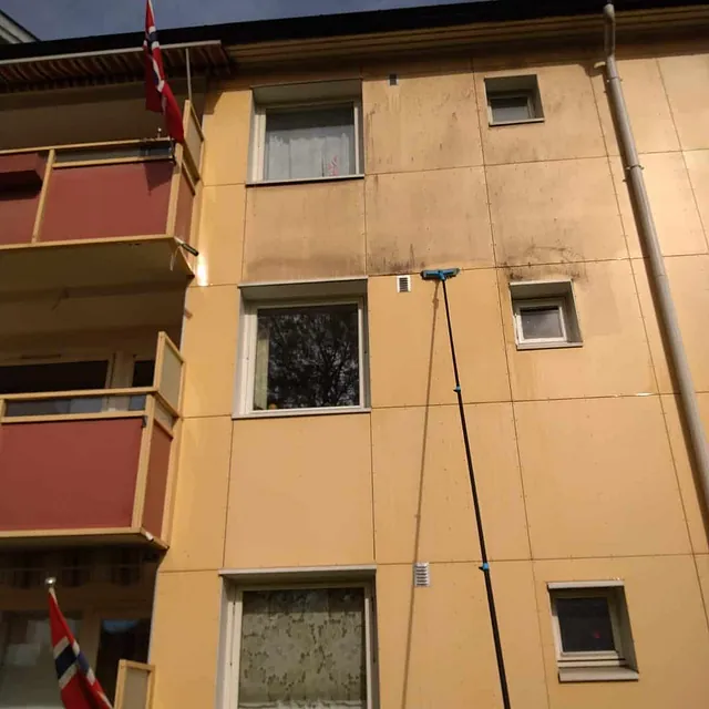 Fasade på boligblokk vaskes med langt teleskopkost, skitten vegg blir gradvis ren.